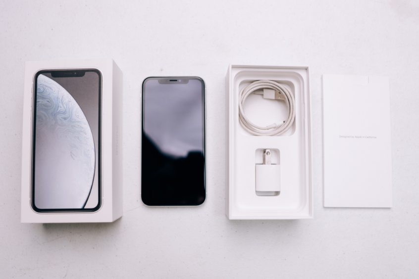 Apple iPhone displayed with its box, charging cable, and power adapter arranged on a white surface