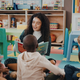 Childcare teacher sits on the floor with a group of children and reads a book to them