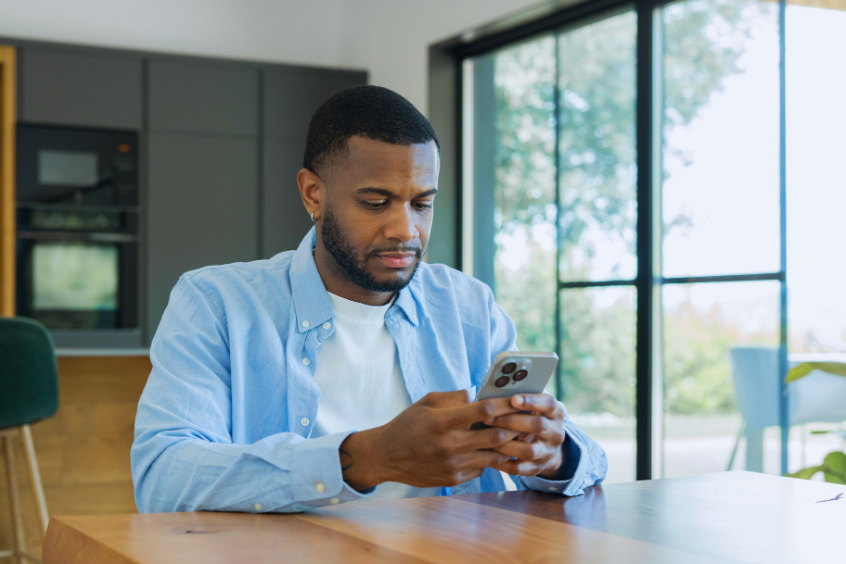 Man sitting at a wooden table intently browsing or checking messages on his mobile phone